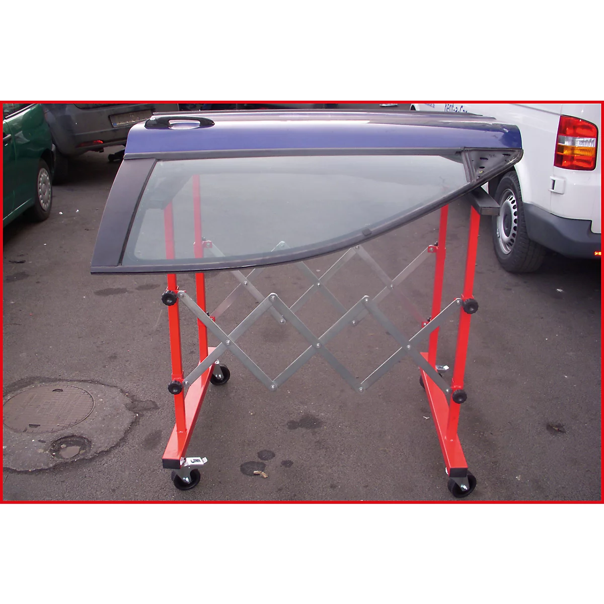 Blaue Autotür auf rotem, ausziehbaren Ständer mit Rädern. Im Hintergrund weitere Autos.